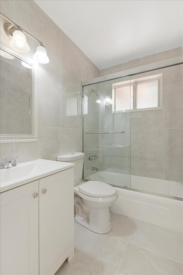 full bath with vanity, tile walls, toilet, combined bath / shower with glass door, and tile patterned floors