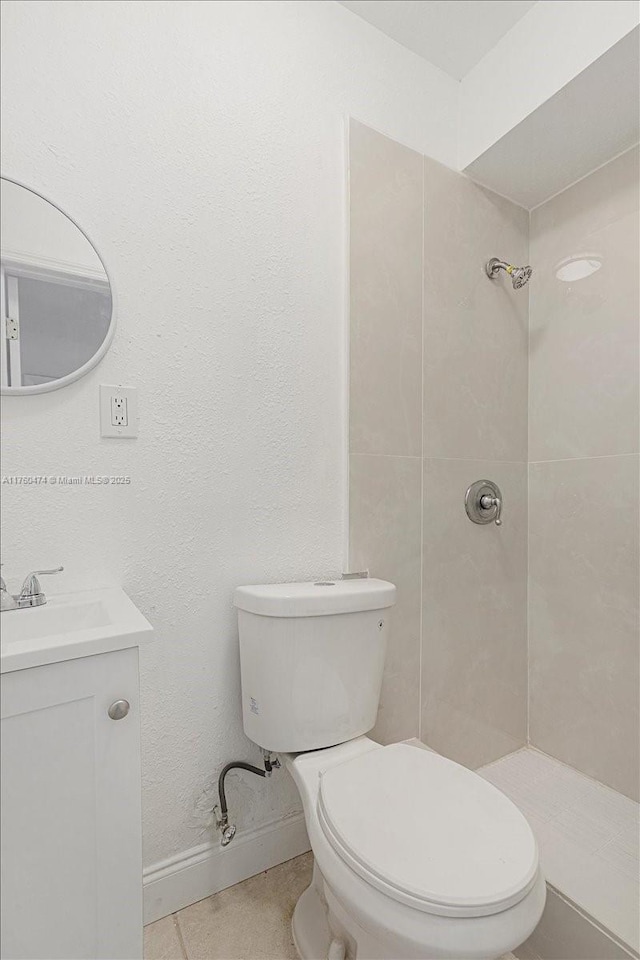 full bathroom featuring baseboards, tiled shower, toilet, and vanity