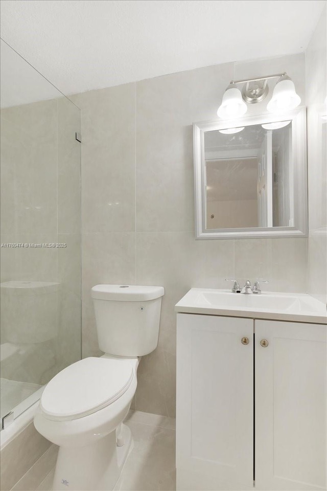 full bathroom with vanity, tile walls, toilet, and tiled shower