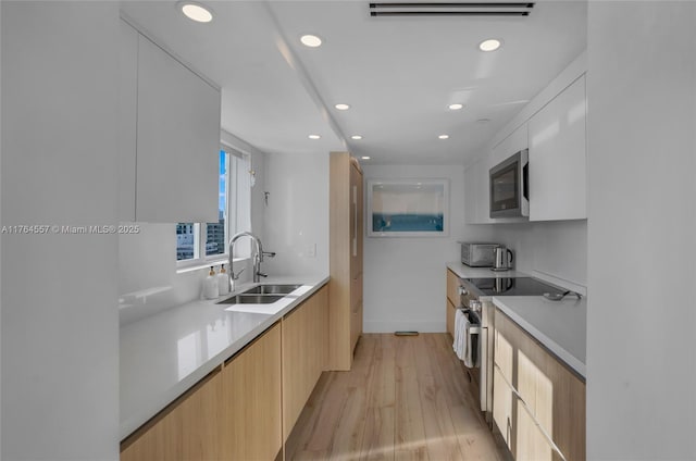 kitchen with light wood finished floors, visible vents, stainless steel appliances, modern cabinets, and a sink