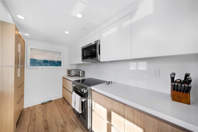 kitchen featuring light countertops, white cabinets, light wood-style floors, appliances with stainless steel finishes, and modern cabinets