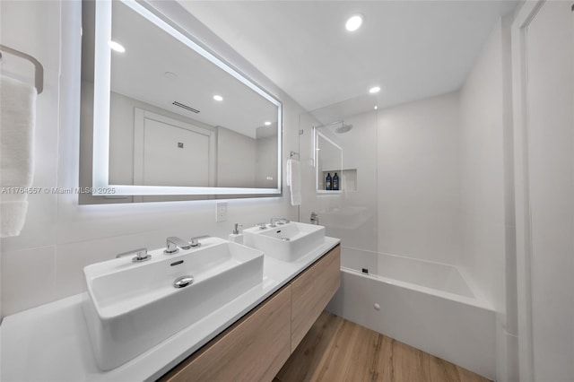 full bathroom with double vanity, wood finished floors, washtub / shower combination, and a sink