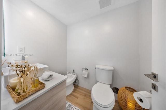 bathroom with visible vents, toilet, wood finished floors, a bidet, and vanity