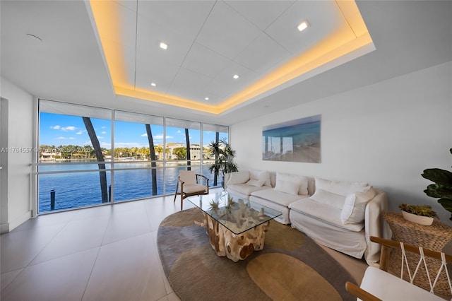 living area with baseboards, a tray ceiling, tile patterned flooring, a water view, and expansive windows