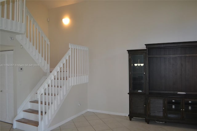 stairway with tile patterned floors, baseboards, and a towering ceiling