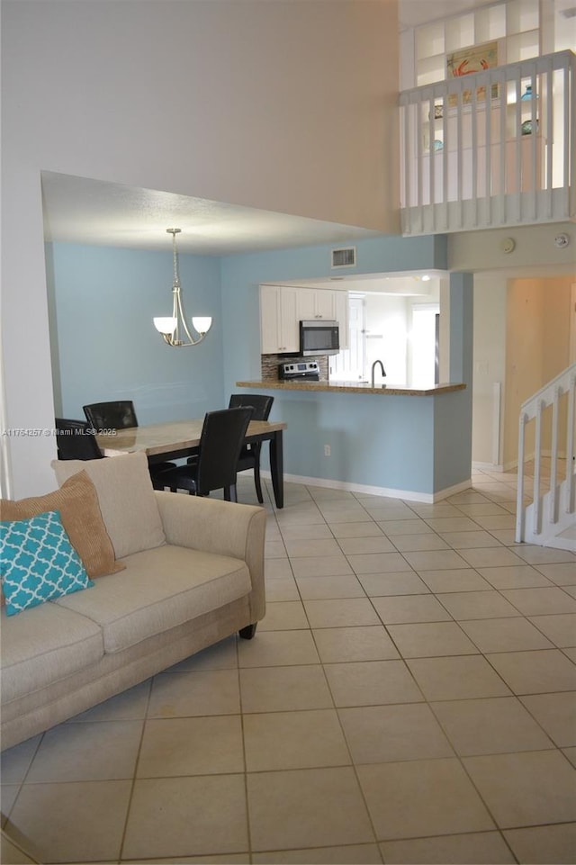 living room featuring baseboards, visible vents, light tile patterned flooring, a towering ceiling, and a notable chandelier