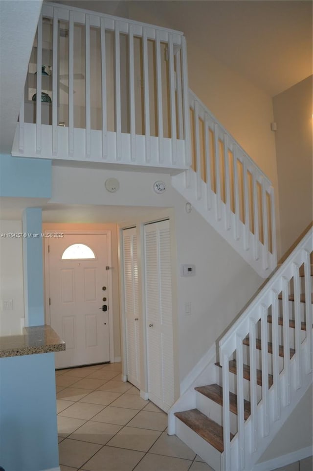 foyer entrance featuring stairway, light tile patterned floors, and a towering ceiling