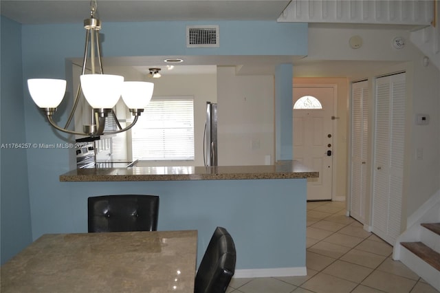 kitchen featuring light tile patterned floors, visible vents, a peninsula, refrigerator, and a notable chandelier