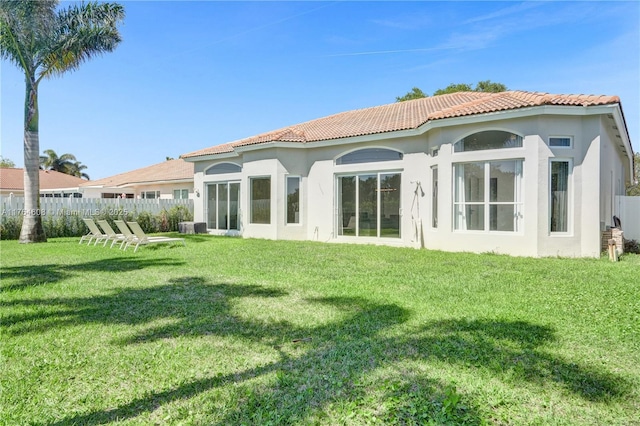 back of property featuring stucco siding, fence, a lawn, and a tiled roof