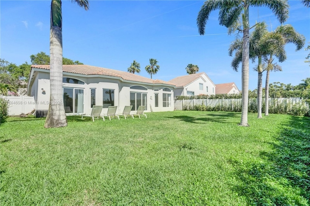 rear view of property featuring a tiled roof, a yard, fence, and stucco siding