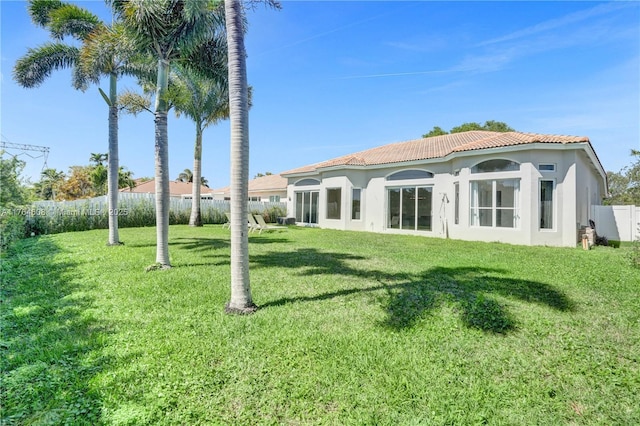 rear view of house with a tile roof, a lawn, fence, and stucco siding