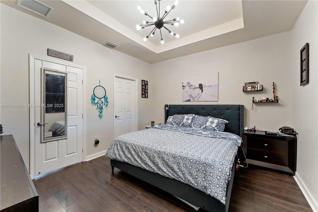 bedroom featuring visible vents, a tray ceiling, wood finished floors, an inviting chandelier, and baseboards