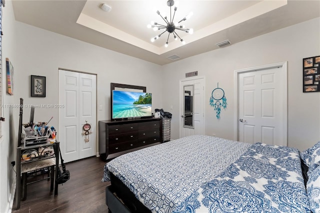 bedroom with dark wood finished floors, visible vents, a raised ceiling, and an inviting chandelier