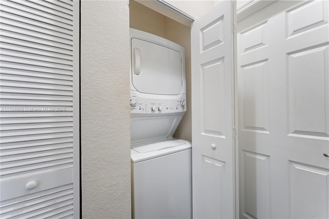 laundry area with stacked washer / drying machine, laundry area, and a textured wall