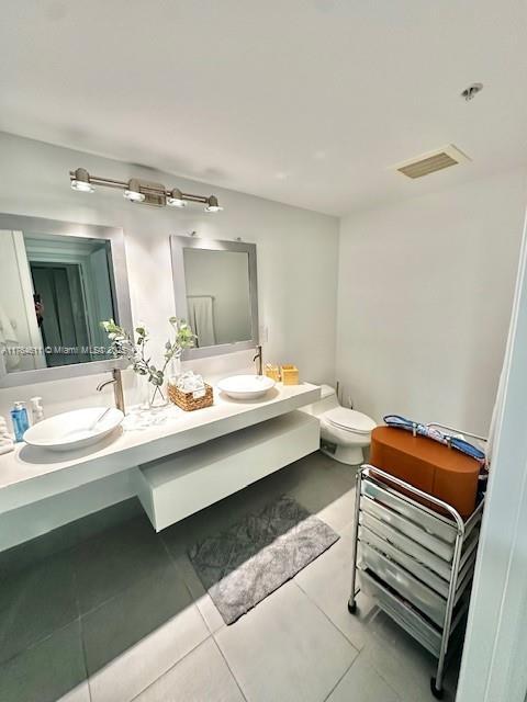 bathroom with visible vents, double vanity, a sink, tile patterned floors, and toilet