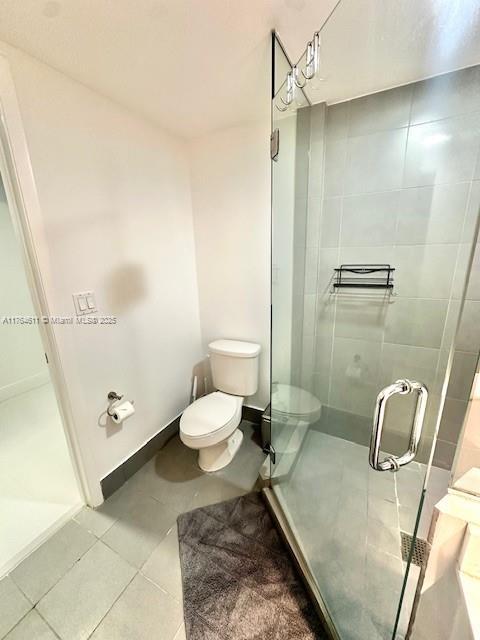 full bath with tile patterned floors, a shower stall, toilet, and baseboards