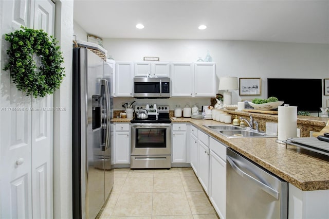 kitchen with a peninsula, light tile patterned flooring, a sink, white cabinets, and appliances with stainless steel finishes