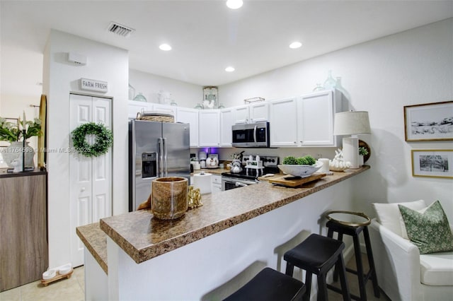 kitchen with visible vents, a breakfast bar, a peninsula, stainless steel appliances, and white cabinetry