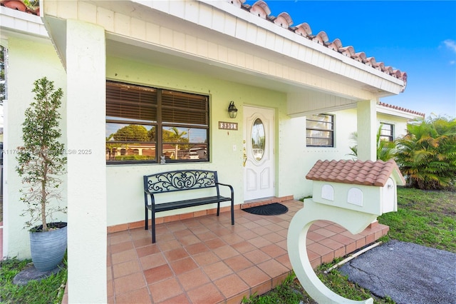 view of exterior entry featuring stucco siding, covered porch, and a tiled roof