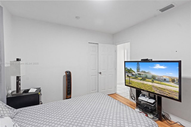 bedroom with wood finished floors, visible vents, and a closet