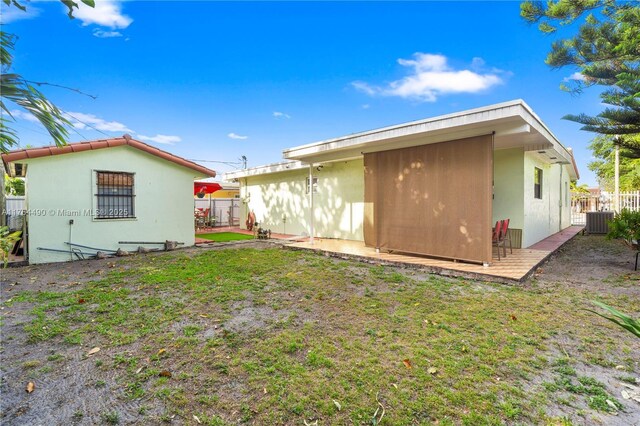 rear view of house featuring central AC unit, fence, and a lawn