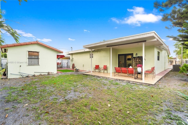 rear view of house featuring stucco siding, central AC unit, a lawn, and fence