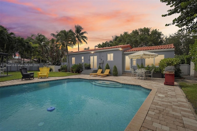 back of house at dusk featuring a fenced in pool, fence, stucco siding, a tile roof, and a patio area