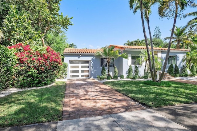 mediterranean / spanish house featuring stucco siding, a front lawn, decorative driveway, an attached garage, and a tiled roof