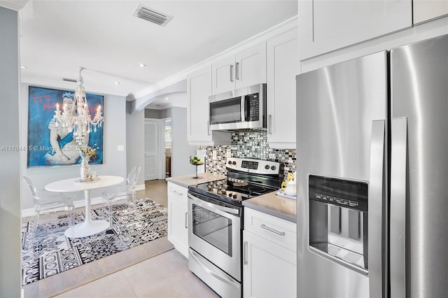 kitchen featuring visible vents, stainless steel appliances, arched walkways, light countertops, and decorative backsplash