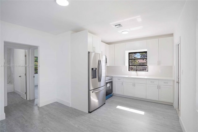 kitchen featuring visible vents, light wood-style flooring, a sink, white cabinetry, and stainless steel appliances