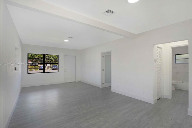 unfurnished room featuring beam ceiling, visible vents, baseboards, and wood finished floors