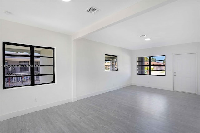 empty room featuring visible vents, beamed ceiling, wood finished floors, and baseboards