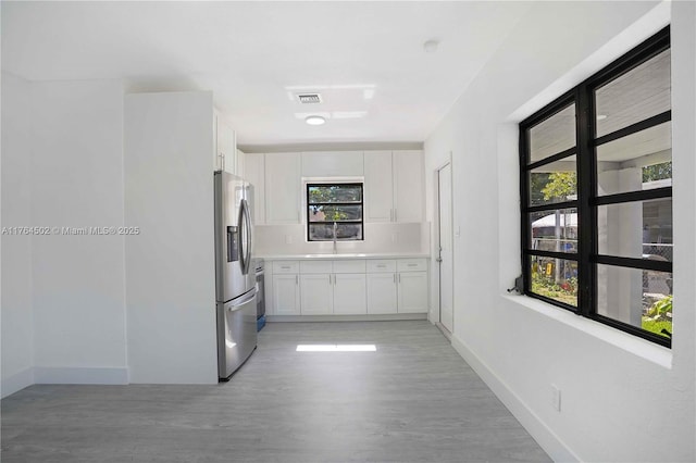 kitchen with stainless steel refrigerator with ice dispenser, a sink, white cabinetry, light countertops, and baseboards