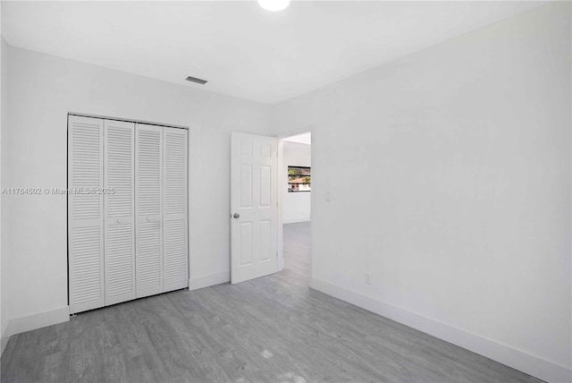 unfurnished bedroom with a closet, visible vents, baseboards, and wood finished floors