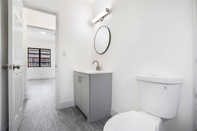 bathroom with baseboards, toilet, wood finished floors, and vanity