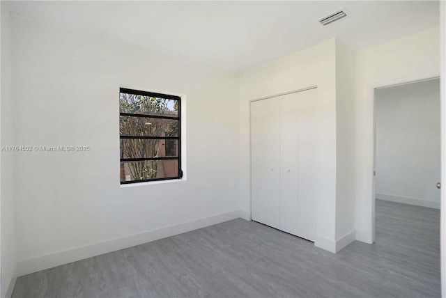 unfurnished bedroom featuring a closet, visible vents, baseboards, and wood finished floors