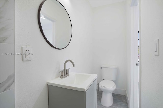 bathroom featuring baseboards, toilet, wood finished floors, and vanity