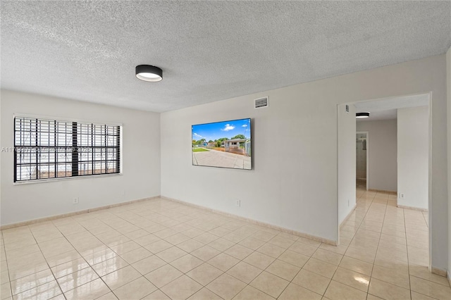 empty room with light tile patterned floors, a textured ceiling, and baseboards