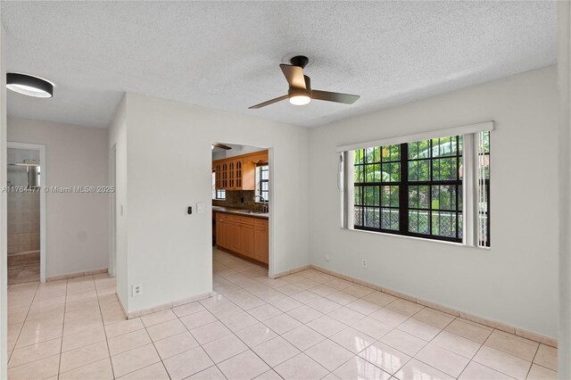 spare room featuring a ceiling fan, a sink, a textured ceiling, light tile patterned flooring, and baseboards