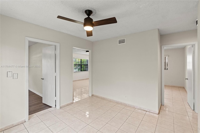 unfurnished room featuring visible vents, baseboards, light tile patterned floors, a textured ceiling, and a ceiling fan