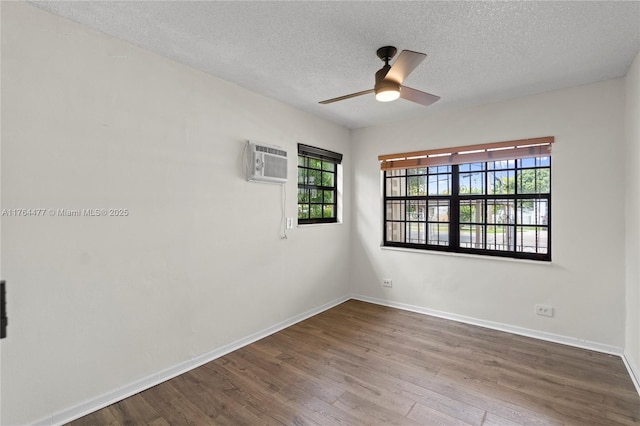 unfurnished room with baseboards, a wall unit AC, wood finished floors, a textured ceiling, and a ceiling fan