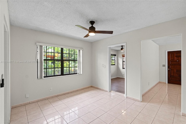 empty room with baseboards, a textured ceiling, ceiling fan, and light tile patterned flooring