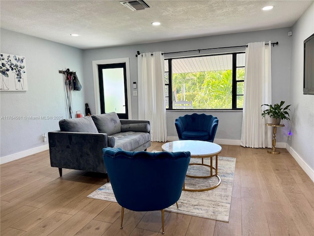 living area featuring visible vents, baseboards, a textured ceiling, and light wood-style flooring