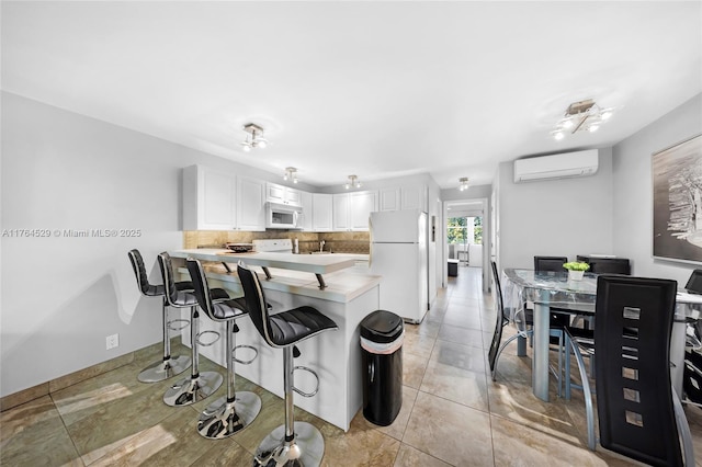 kitchen with an AC wall unit, a breakfast bar, backsplash, white appliances, and a peninsula