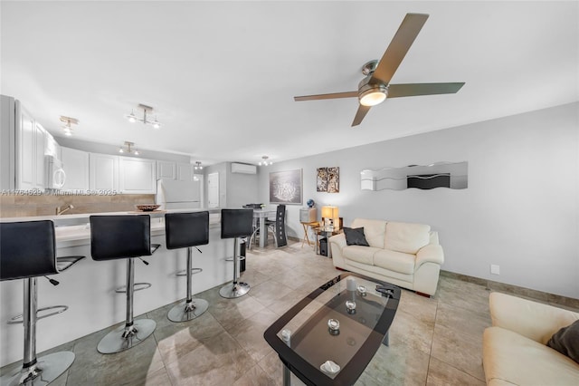 living room featuring a wall unit AC, light tile patterned floors, baseboards, and ceiling fan