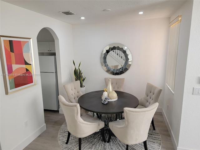 dining space with arched walkways, visible vents, light wood-style flooring, and baseboards