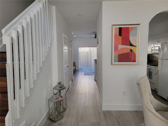 hallway featuring baseboards, stairs, recessed lighting, light wood-style floors, and arched walkways