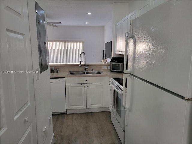 kitchen with light countertops, wood finished floors, white cabinets, white appliances, and a sink