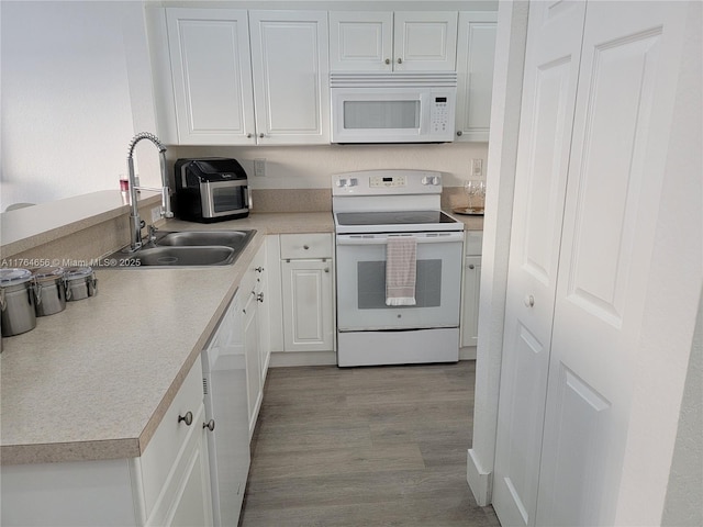 kitchen featuring white cabinets, white appliances, light countertops, and a sink