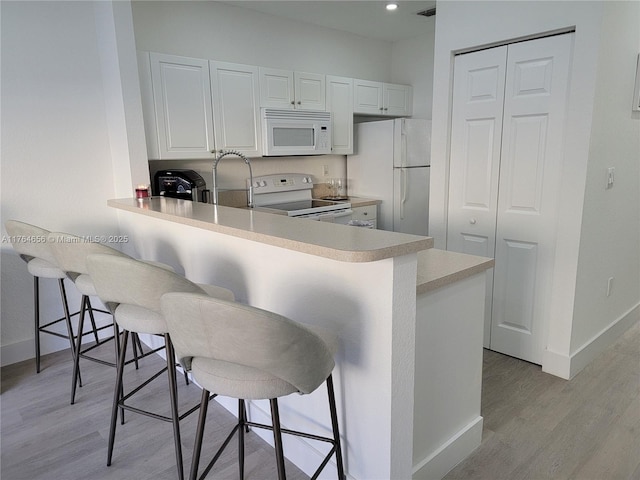 kitchen with a kitchen bar, white appliances, light wood-style flooring, and a peninsula